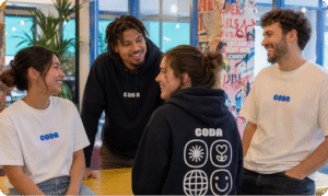Four Coda team members wearing Coda-branded clothing chat and smile together in a bright office.